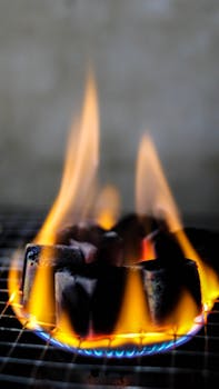 Burning charcoal cubes on a grill with vibrant flames in vertical orientation.