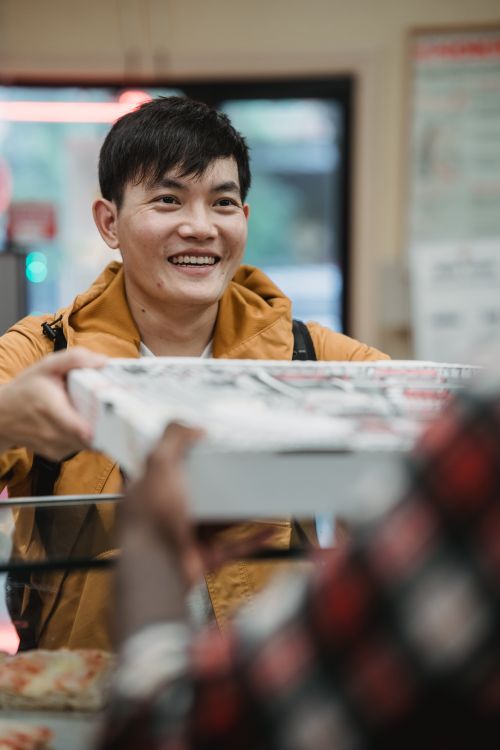 Free A cheerful man receives a takeaway pizza order in a restaurant setting, showcasing a happy dining experience. Stock Photo