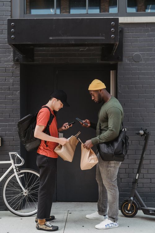 Free Two delivery men exchanging packages and using smartphones on a city street. Stock Photo