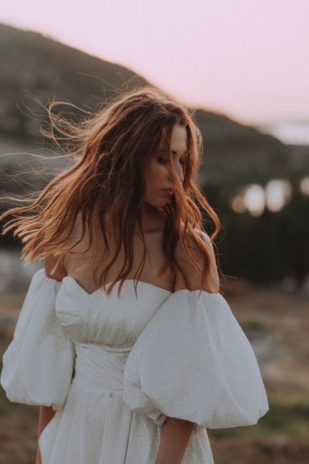A woman in a white off-shoulder dress at sunset with flowing hair outdoors.
