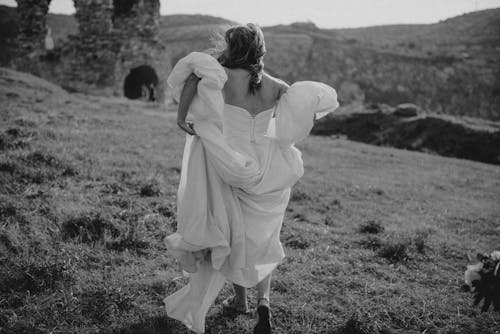 Free Grayscale Photo of a Woman in White Dress Walking on the Grass Field Stock Photo