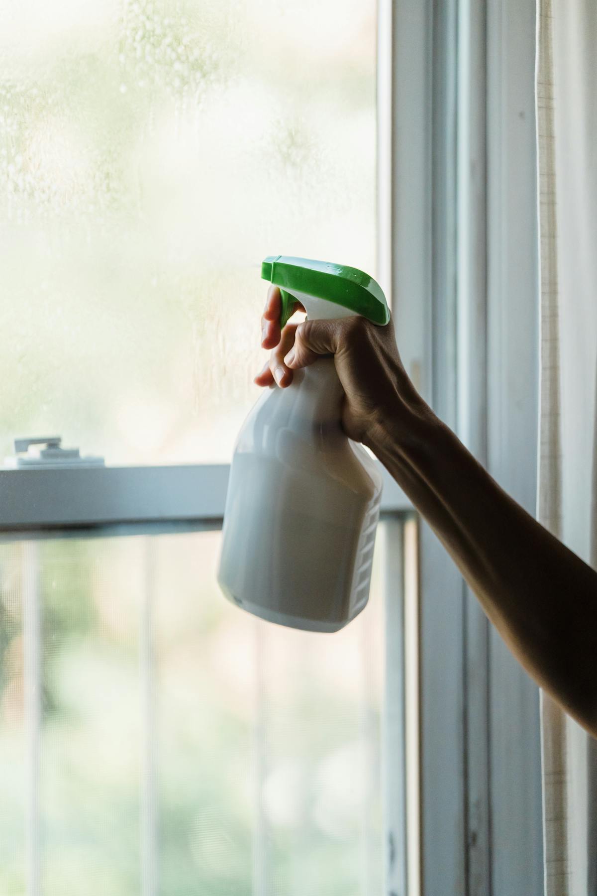 Hand met witte sprayfles met groene nozzle, symbool voor simpele eco schoonmaak.