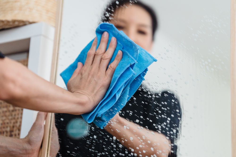 Mà netejant un vidre amb un drap blau i llum natural