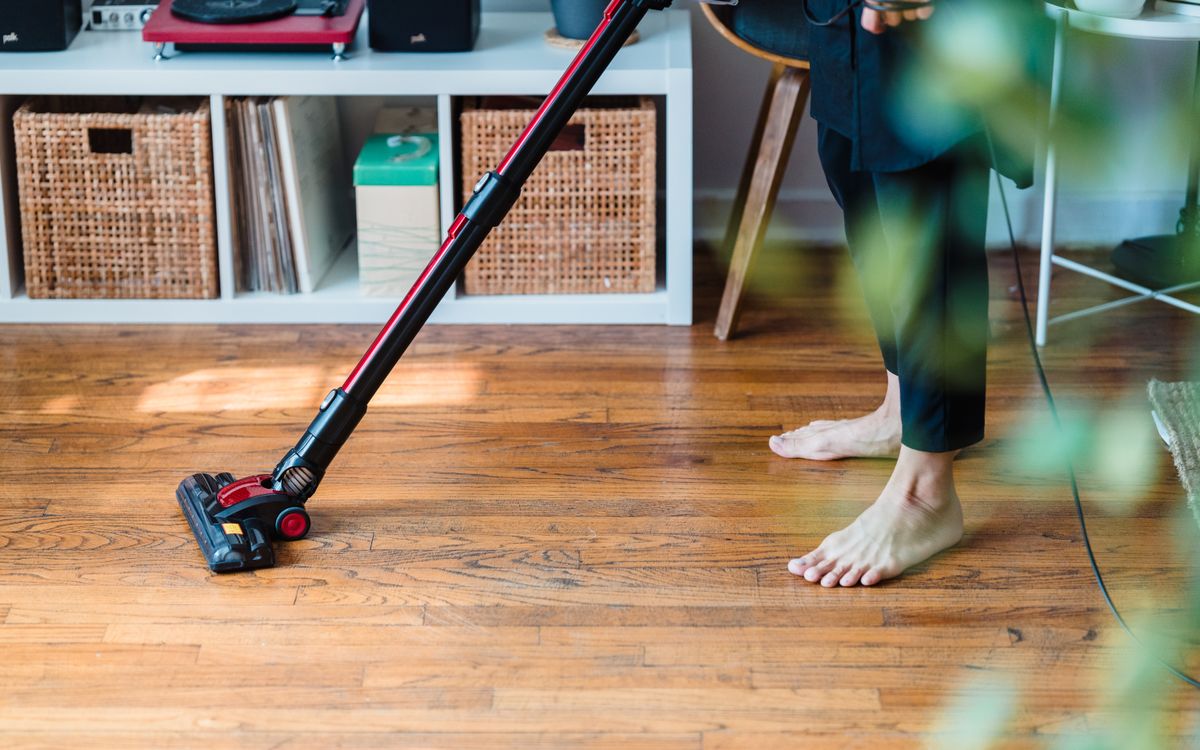 A person vacuuming wooden flooring in a cozy room, emphasizing clean living space.