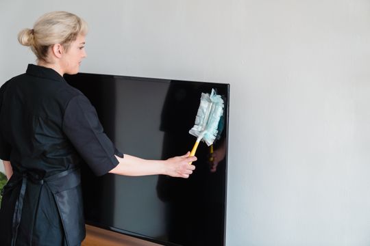 A cleaning professional dusting a home