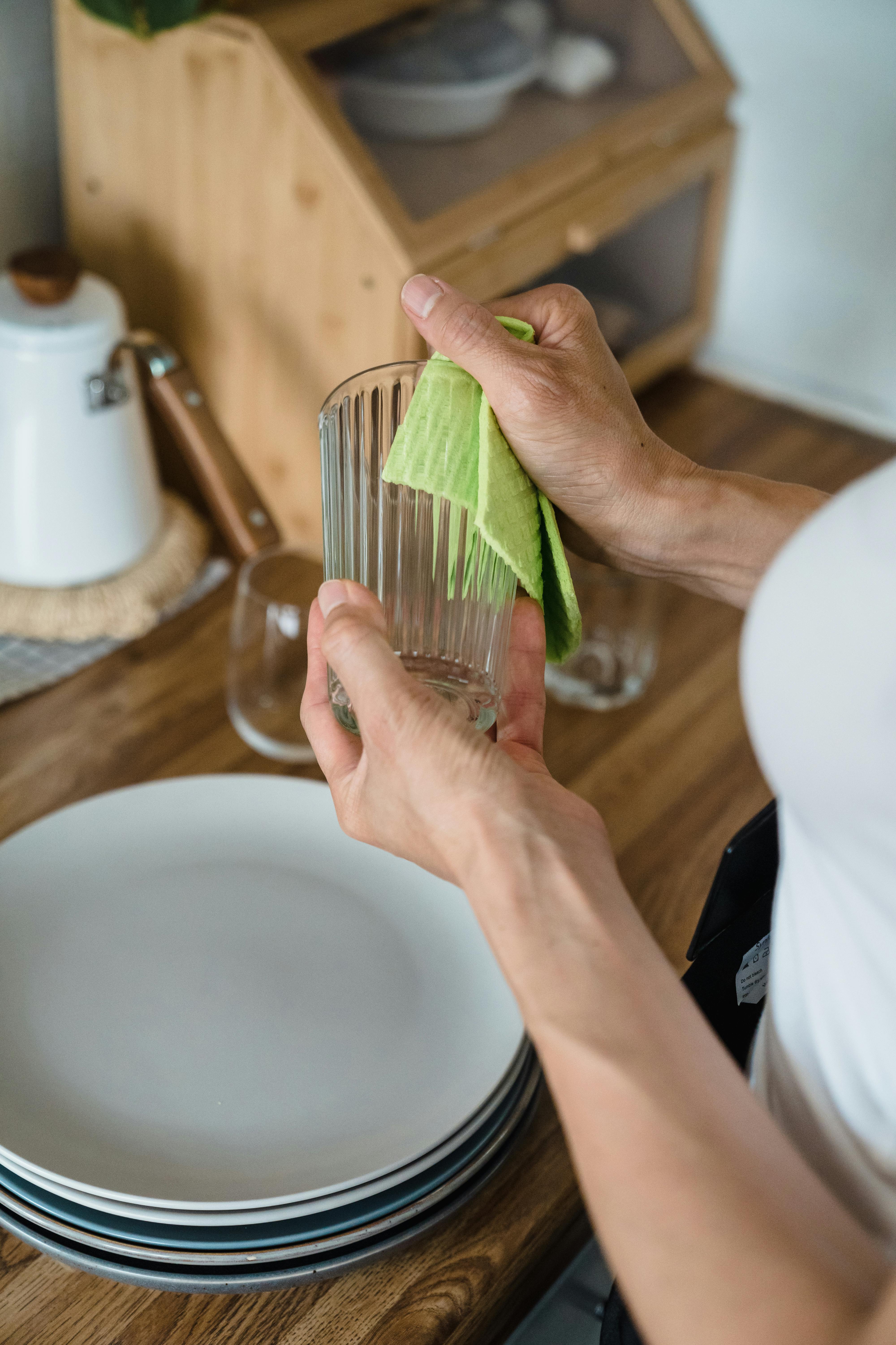Free Close-up of a woman wiping a glass with a cloth in a cozy kitchen environment. Stock Photo