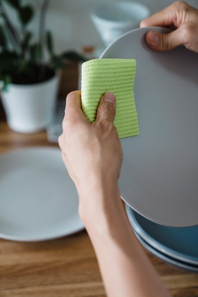 A Person Wiping A Plate With A Cloth