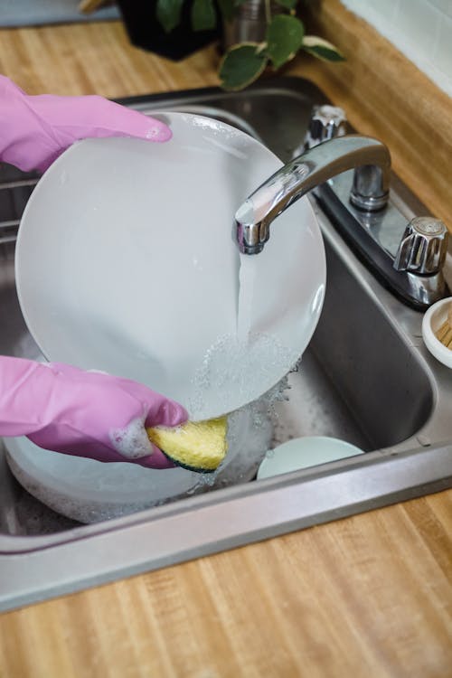 Free A Person Washing a Plate in the Kitchen Sink Stock Photo