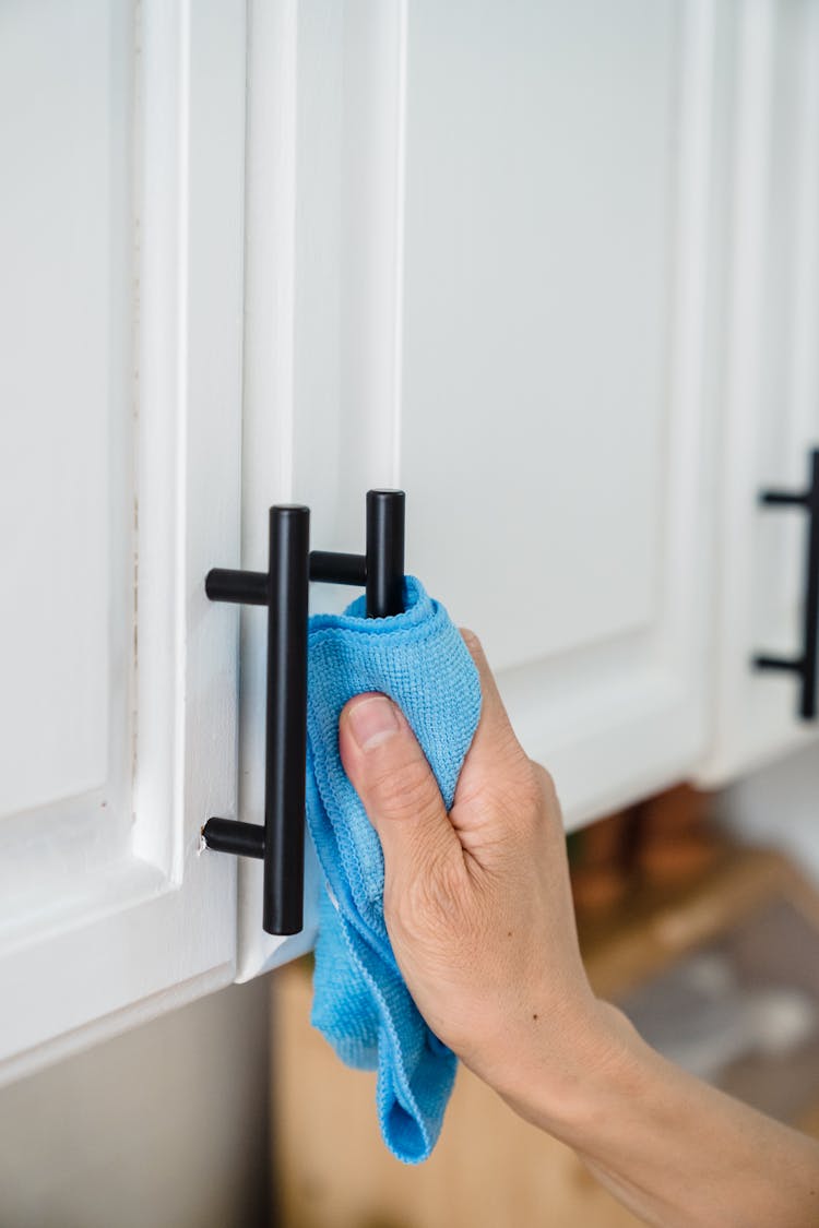 A Person Cleaning The Handles Of Cabinet Using A Rag