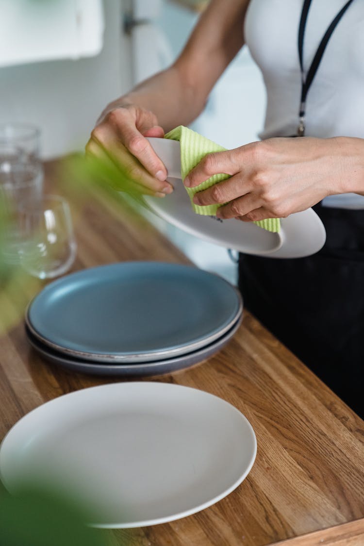 A Person Wiping Plates Using A Cloth