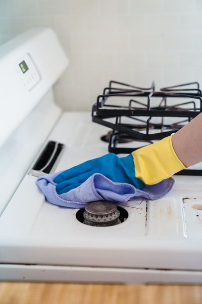 Rubber-gloved hand wiping a white gas stovetop with a purple cloth