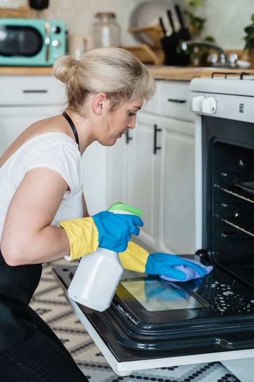Woman in White T-shirt Holding White and Green Plastic Spray Bottle Cleaning the Oven