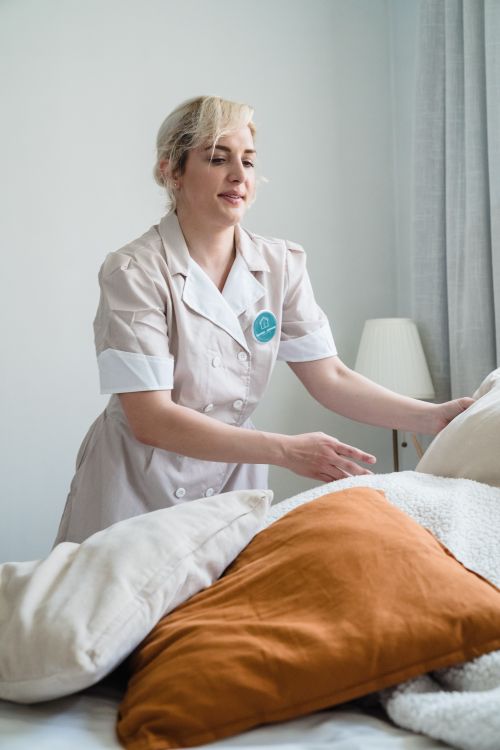 Free A housekeeper in uniform tidying up a bed with multiple pillows in a well-lit room. Stock Photo