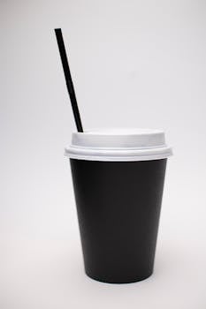 Minimalist black paper cup with a lid and straw on a white background.