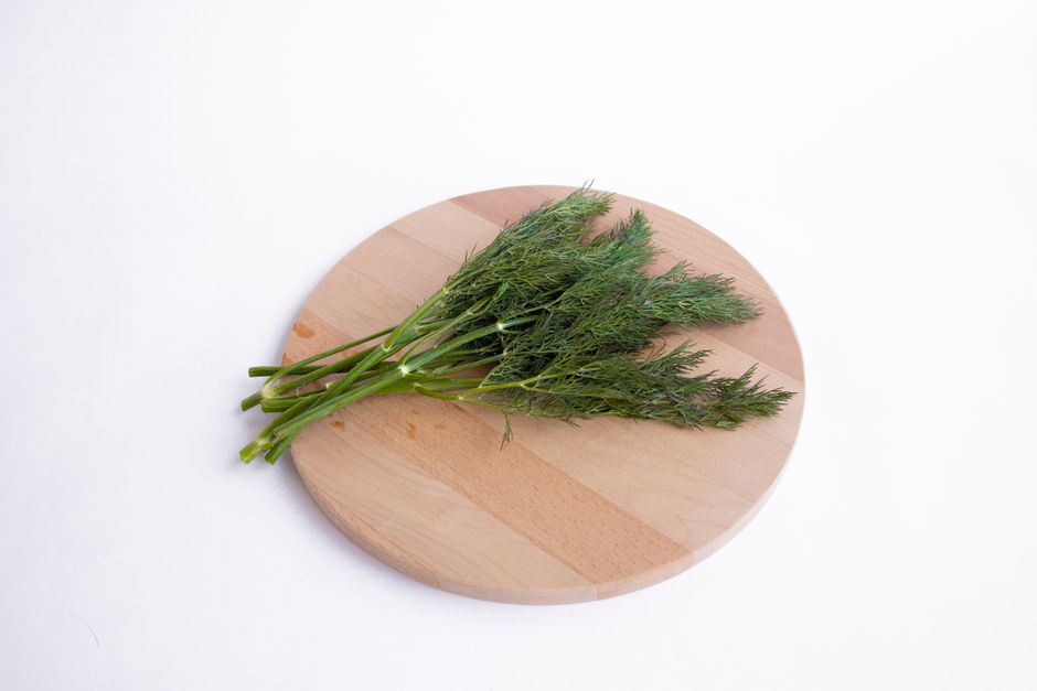 A bunch of feathery fresh dill sprigs with fine, thread-like green leaves on a wooden cutting board.
