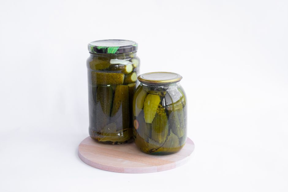 A glass jar of whole fermented cucumber pickles submerged in cloudy brine with dill and garlic cloves visible through the glass.