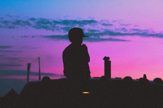 Silhouette of a child sitting on a vehicle against a vibrant purple sunset sky in Krasnodar, Russia.