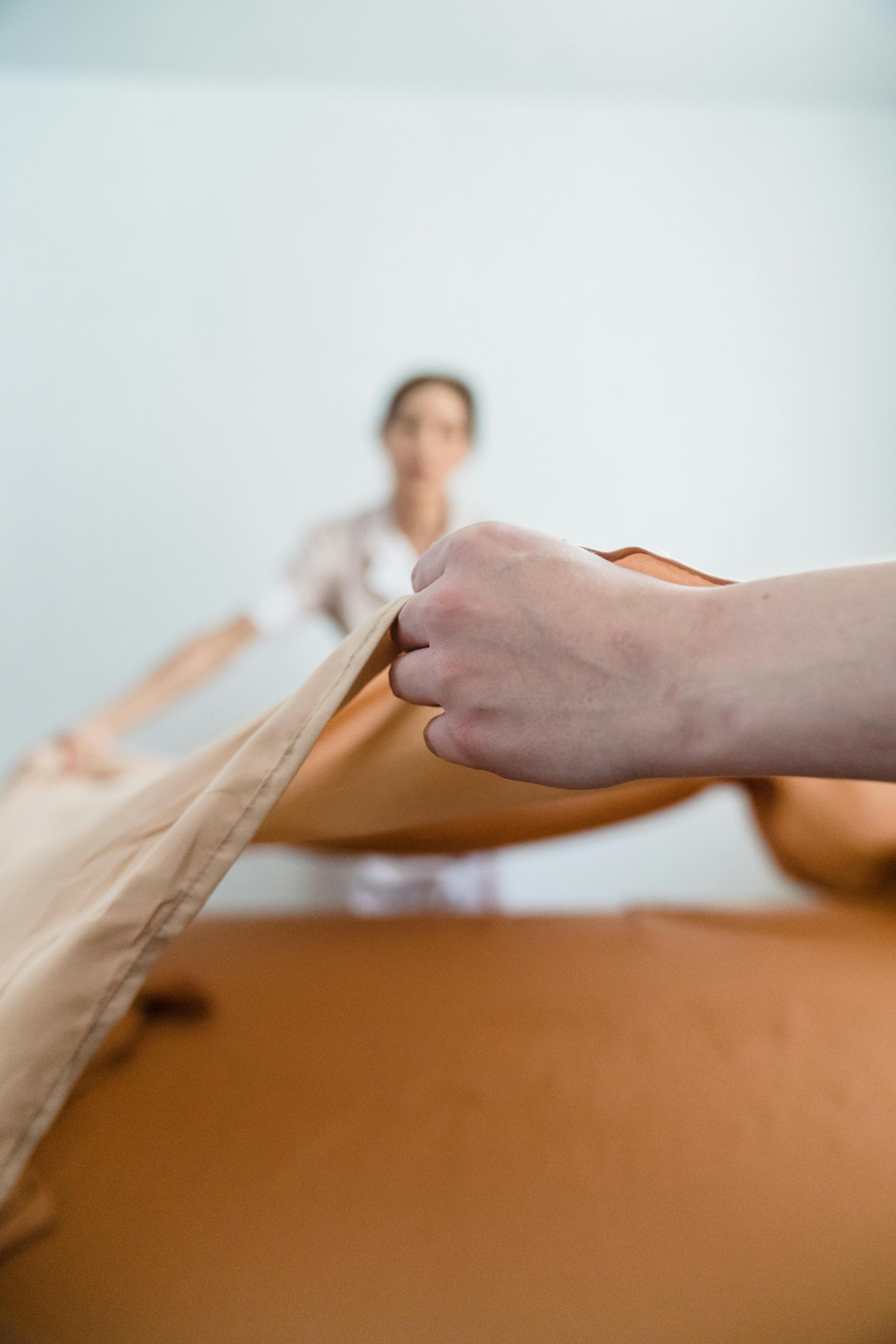 Close-up view of hands spreading a beige bedsheet, creating a warm and tidy atmosphere.