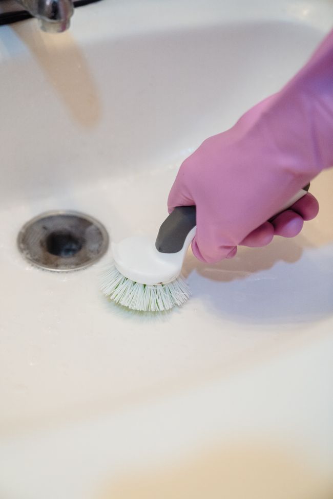 Bathroom sink being cleaned with a scrubbing brush