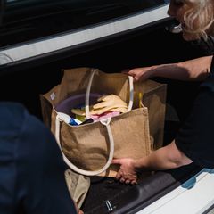 Hands lowering a jute tote full of cleaning bottles and cloths into a car boot