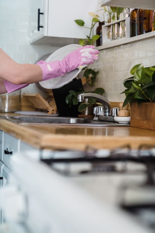 Free A woman uses pink gloves to wash dishes in a modern kitchen environment. Stock Photo
