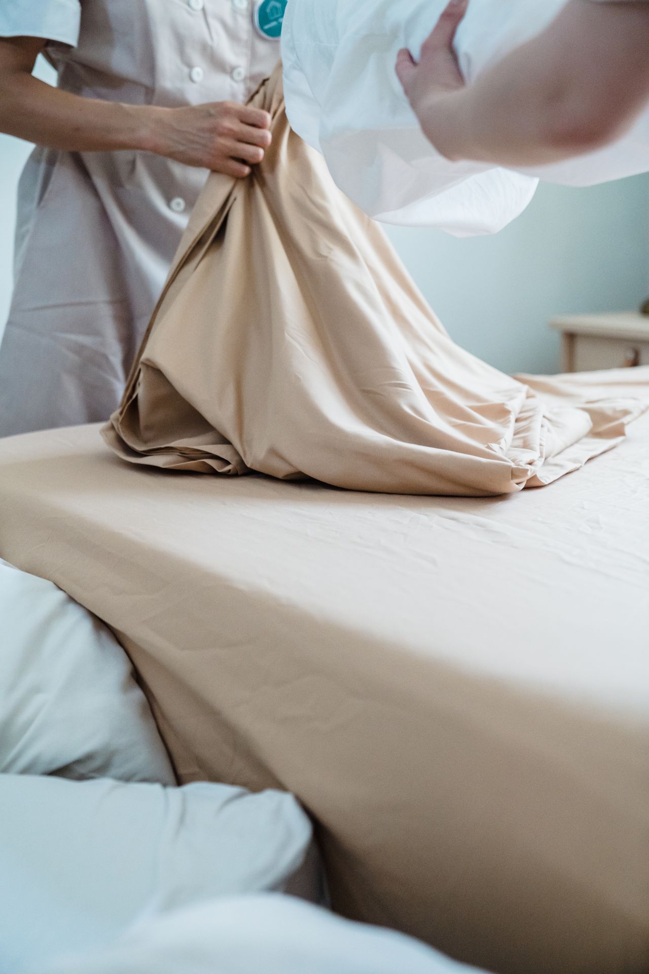 Housekeeper smoothing a beige fitted sheet over a mattress