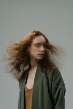 Blurred motion portrait of a redheaded woman in a green jacket, captured indoors.