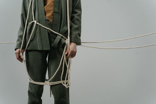 Free A captivating conceptual photograph showing a person in green clothes tangled with ropes, symbolizing entrapment or struggle. Stock Photo