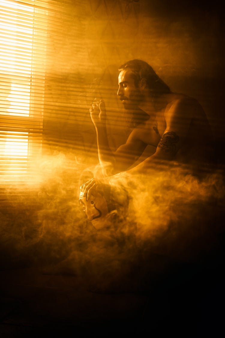 Light Illuminating Man Sitting In Room Filled With Smoke