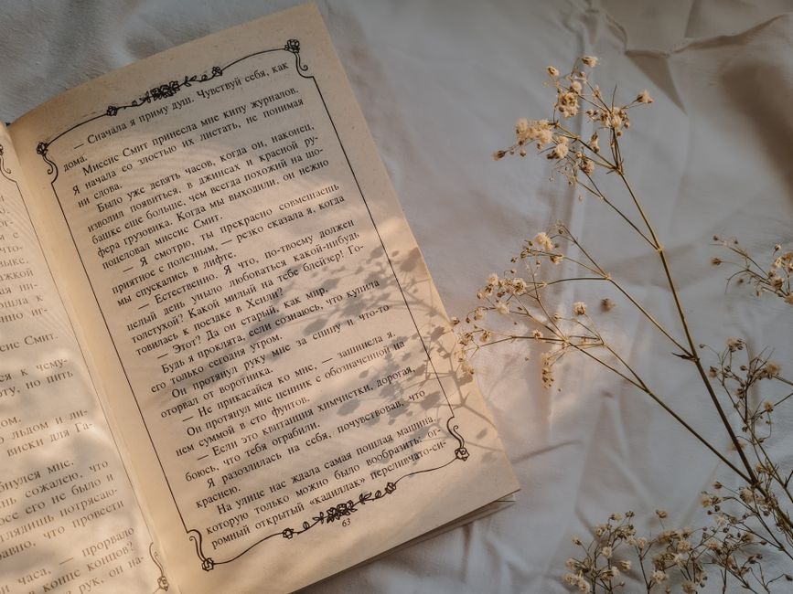 Open book on a soft bedsheet with gypsophila flowers gently placed beside it.