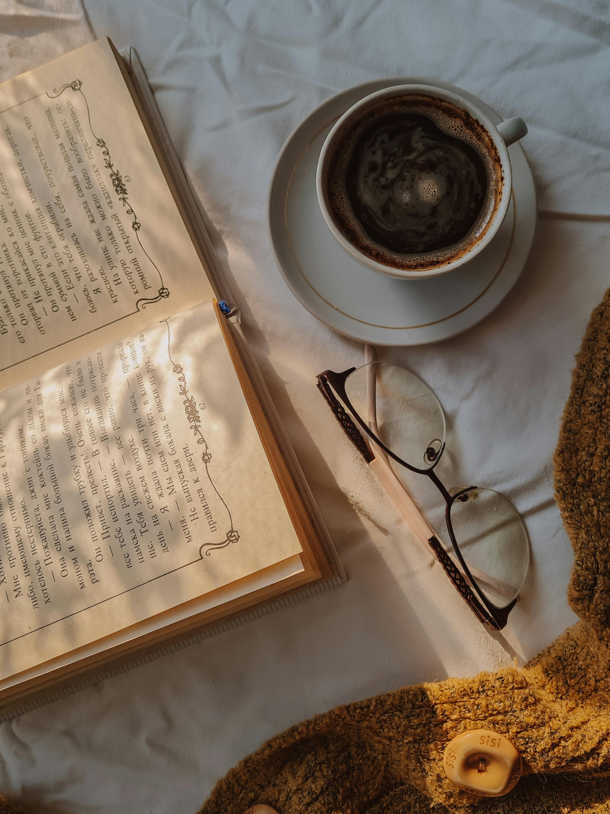 An inviting setup of coffee, book, and eyeglasses on a warm-toned surface, perfect for a quiet afternoon.