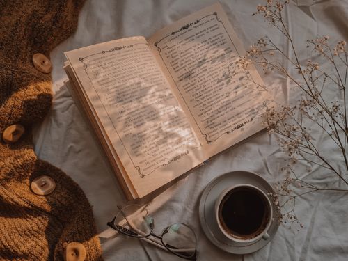 Free Warm flat lay image featuring an open book, coffee, and dried flowers on a cozy fabric background. Stock Photo