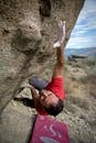 一个穿着红色衬衫的男人在陡峭的岩石上抱石，展现了力量和决心