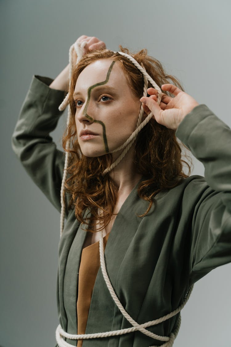 Conceptual Photo Of A Woman Tied With A Rope And With A Line Painted On Her Face