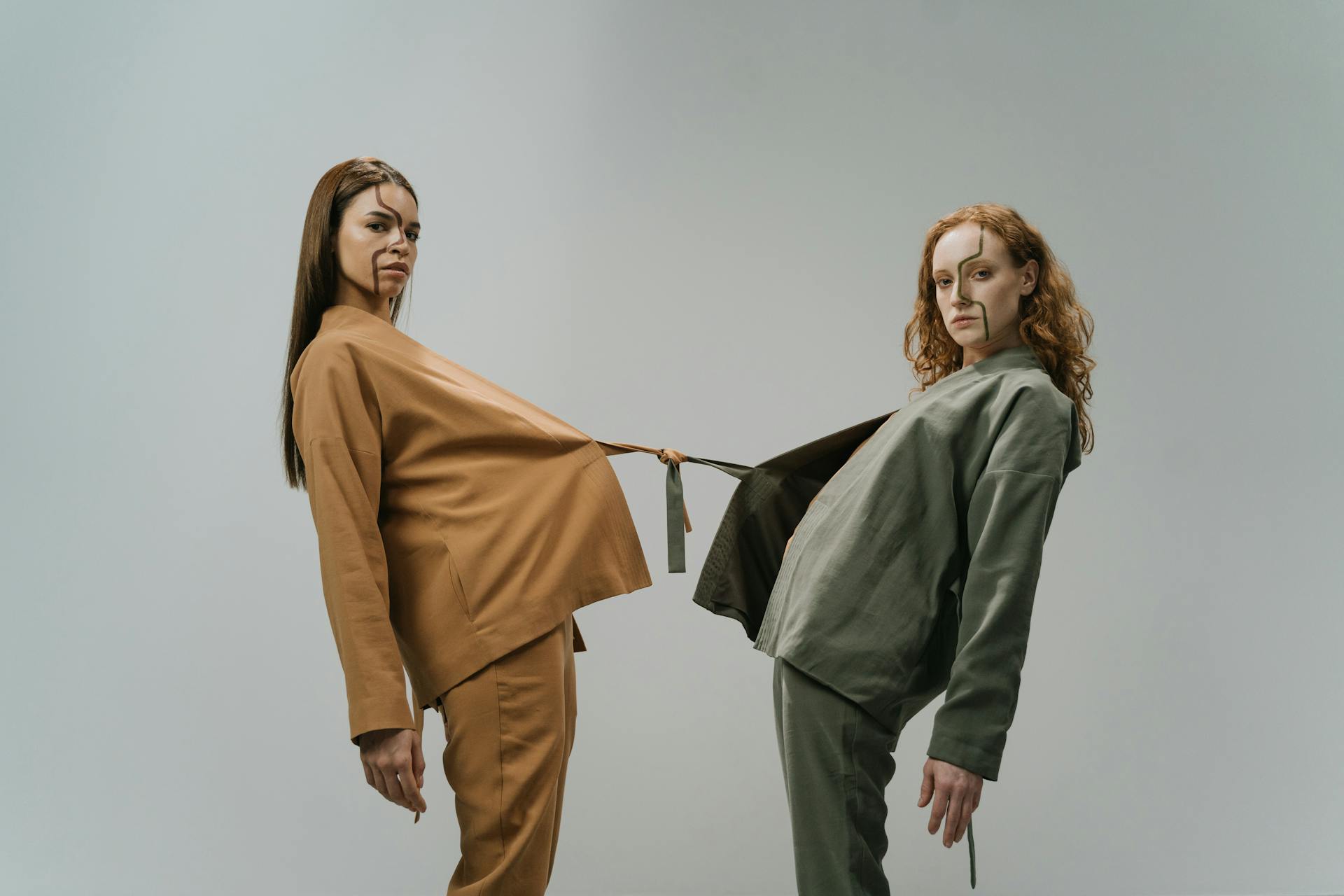 Creative studio portrait of two women in fashionable outfits linked by clothing.