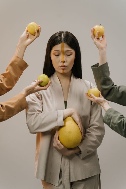Free A serene woman with face paint holds a pomelo surrounded by hands presenting apples. Stock Photo