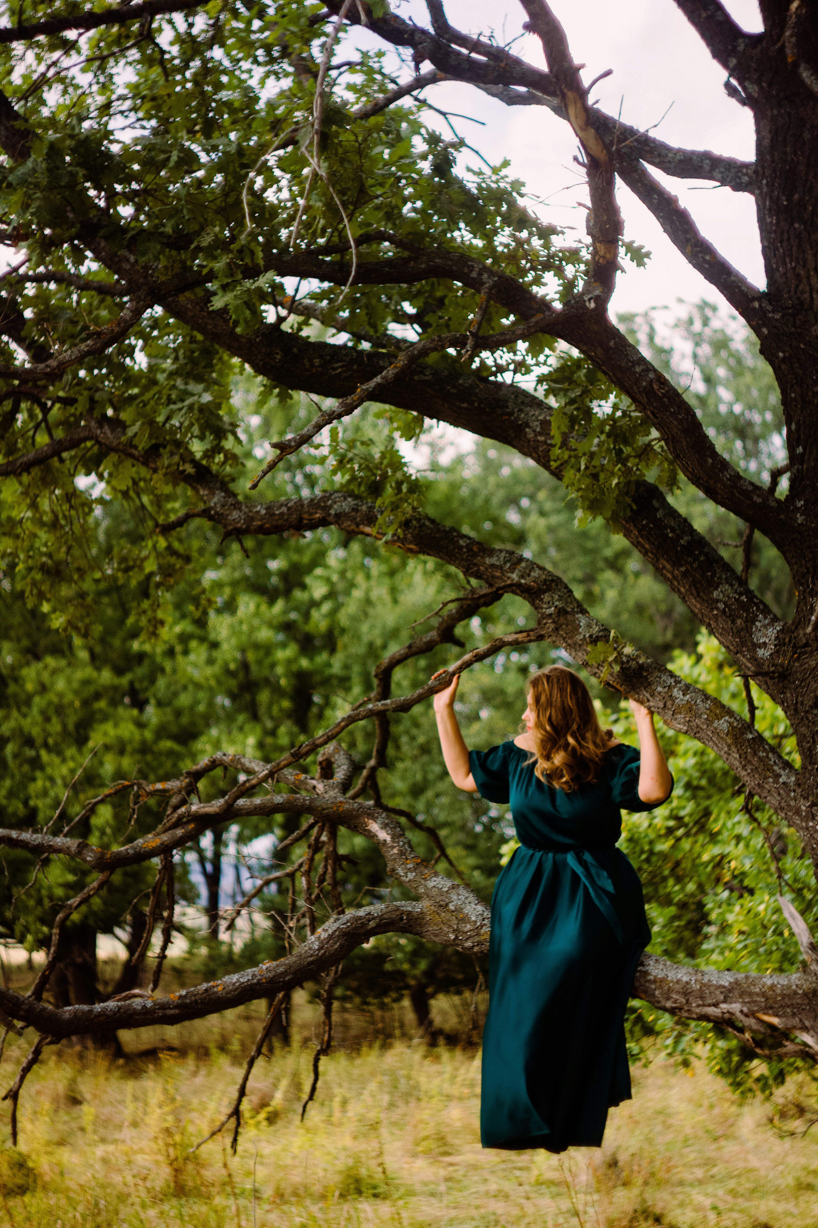 Woman Wearing a Green Dress Sitting on Tree Branch Looking Sideways  Free  Stock Photo