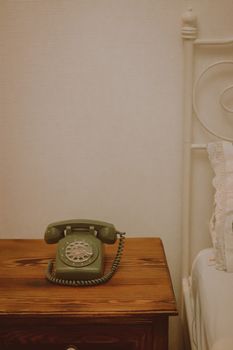 Retro green rotary phone on a wooden bedside table in a vintage-styled bedroom setting.
