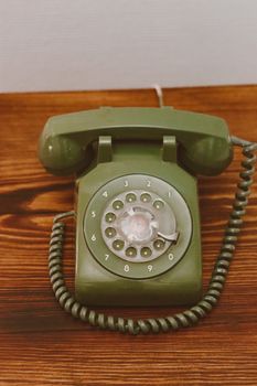 A classic olive green rotary dial telephone showcasing retro design on a wooden surface.