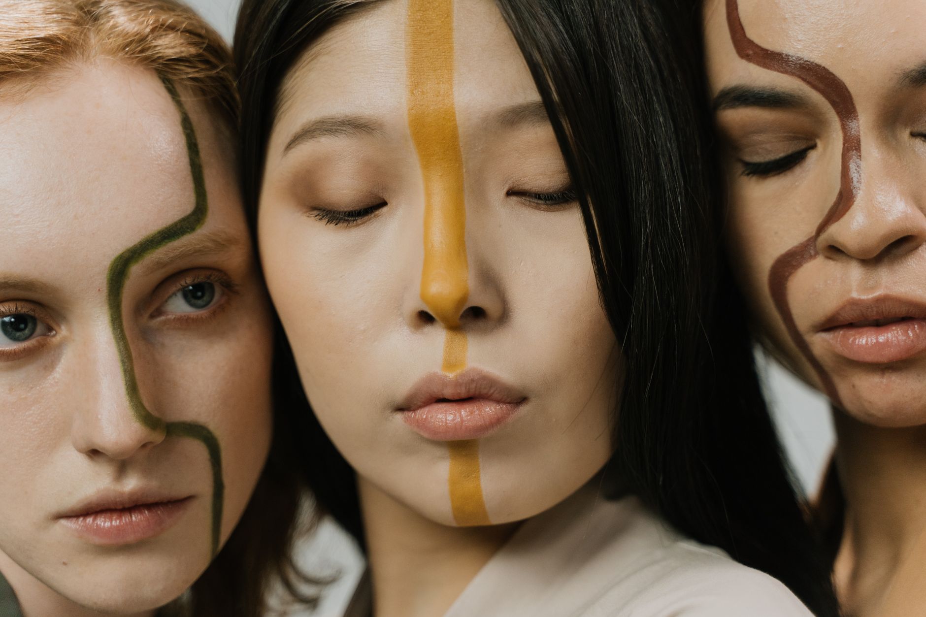 Three women with face paint illustrating diversity in a stylish studio portrait.