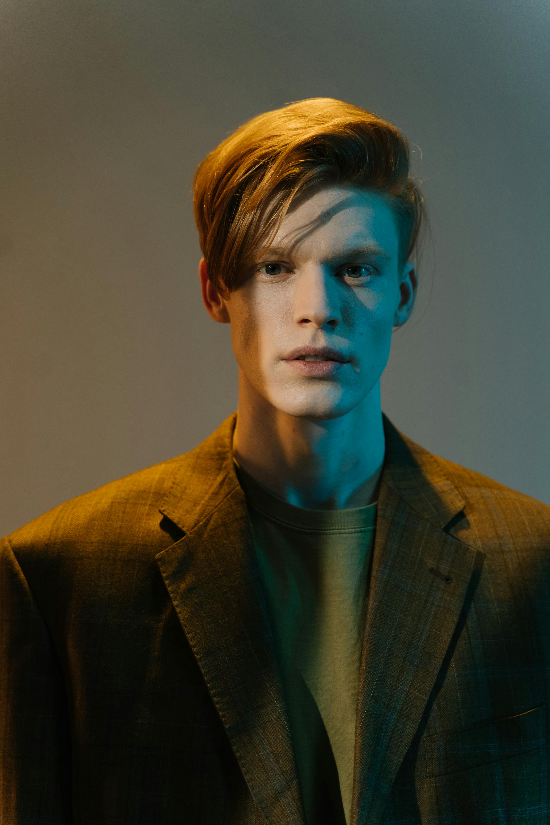 A fashionable young man in a suit, captured in a studio setting with a moody lighting effect, blending warm and cool tones.