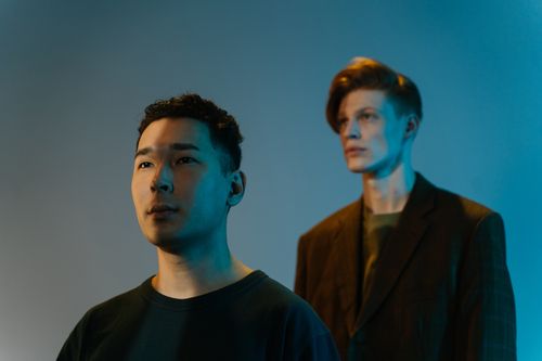 Free Portrait of two men in a studio with artistic blue and orange lighting, showcasing creative contrast. Stock Photo