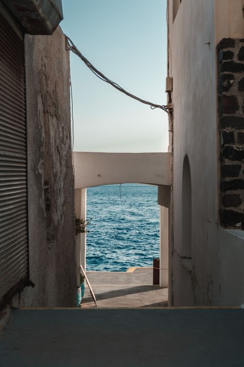 Free A tranquil view of the ocean through a coastal alley archway. Ideal for travel and architecture themes. Stock Photo