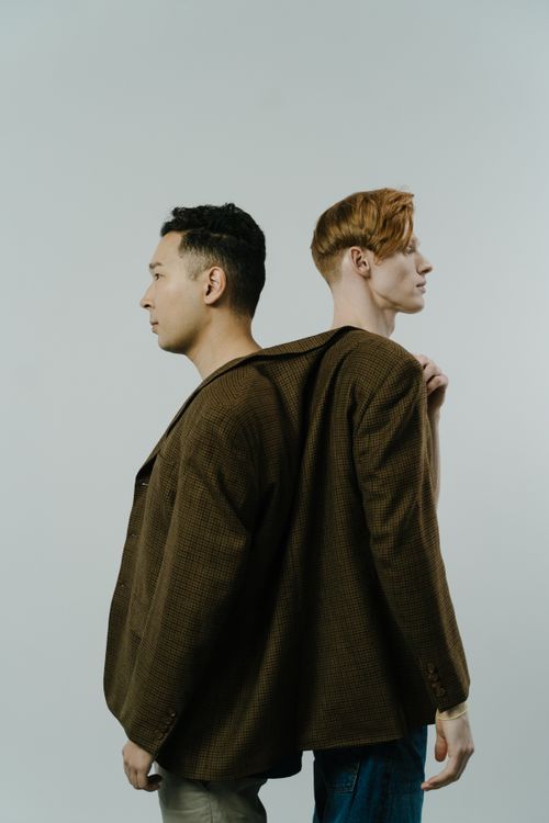 Free Conceptual portrait of two young men in a studio, standing back to back, sharing a single blazer. Stock Photo