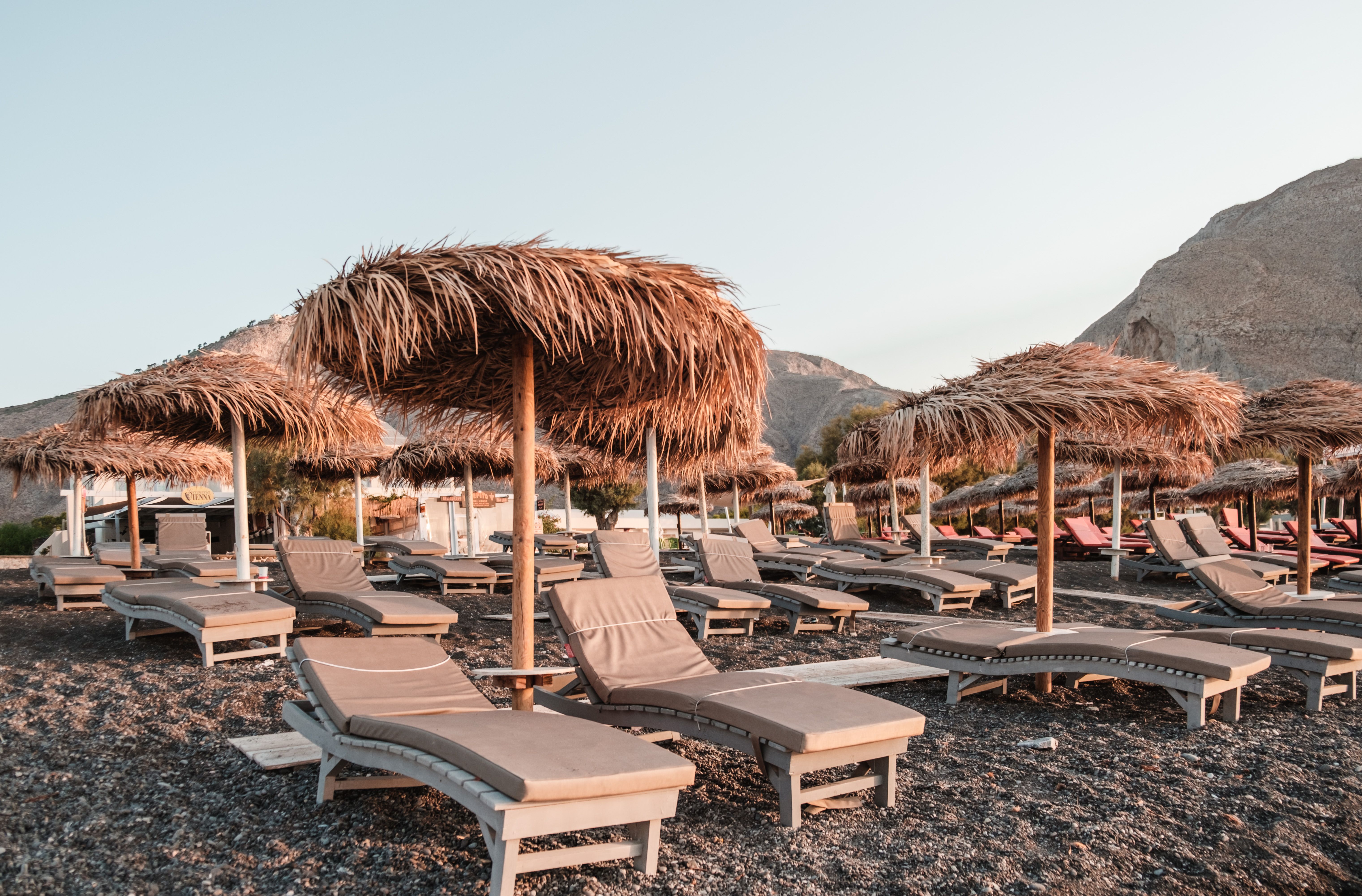 Peaceful beach setting with straw umbrellas and sun loungers on rocky shore.