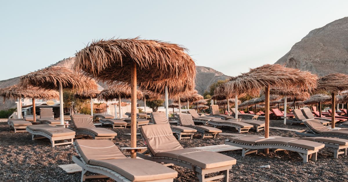 Peaceful beach setting with straw umbrellas and sun loungers on rocky shore.