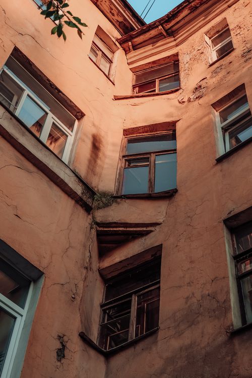 Free Weathered building exterior with sunlight casting shadows on peeling walls and windows. Stock Photo