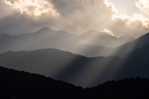 Free Silhouetted mountains under dramatic clouds with sun rays breaking through. Stock Photo
