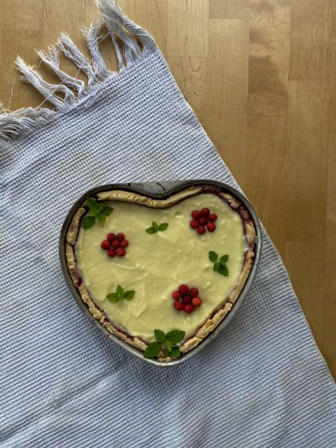 Delicious heart-shaped pastry with raspberries and mint leaves on a textured surface.