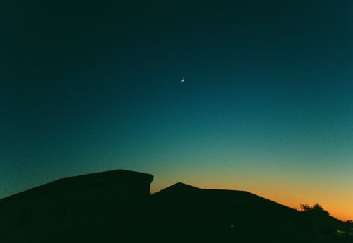 Free Silhouette of houses against a vibrant crescent moon sky during evening twilight, showcasing a peaceful urban landscape. Stock Photo
